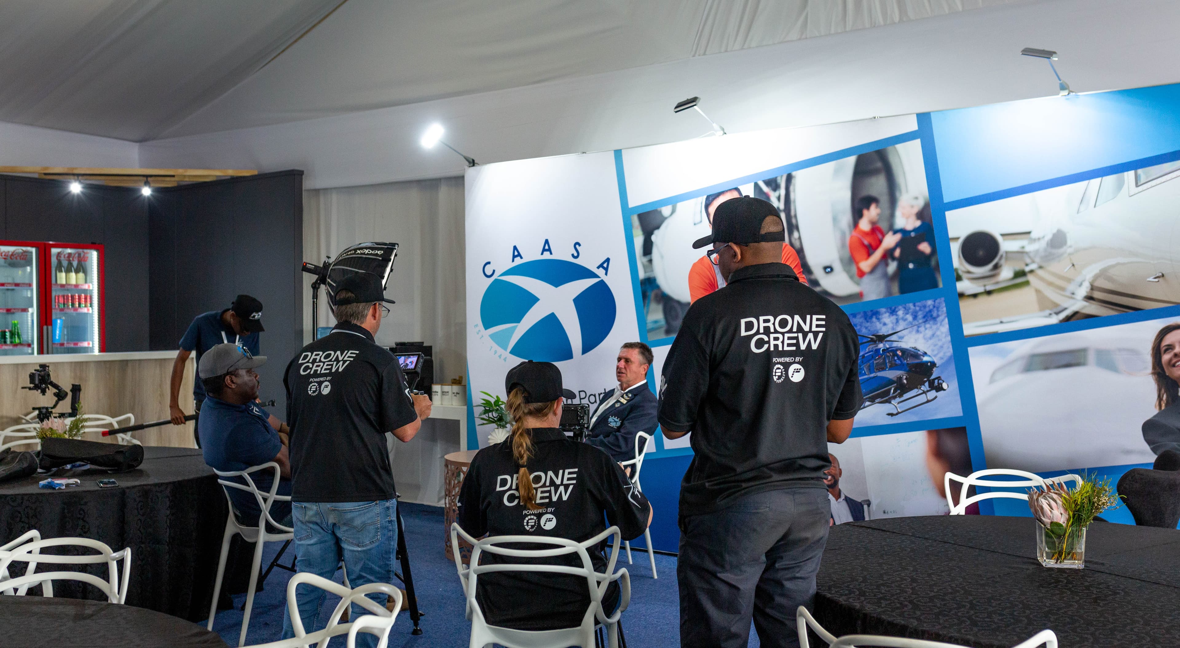 Drone crew members film an interview in front of a CAASA aviation-themed backdrop.